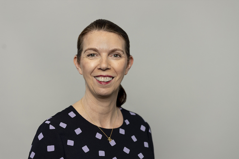 Angela MacDonald, smiling and wearing a navy top, against a grey background